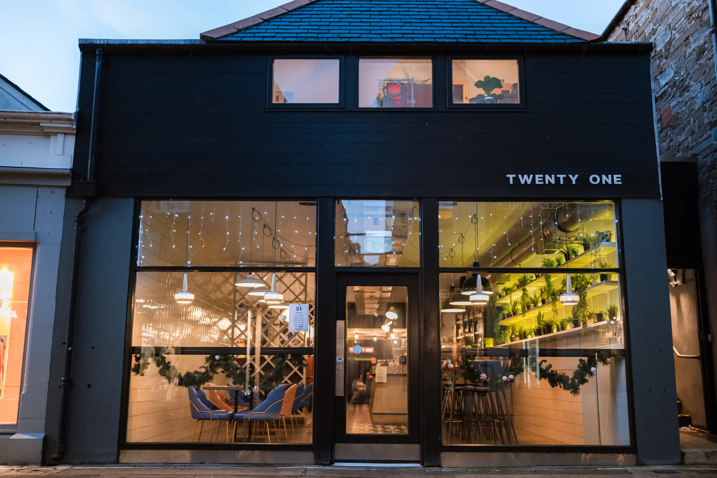 The Twenty One shopfront at dusk, lit from inside
